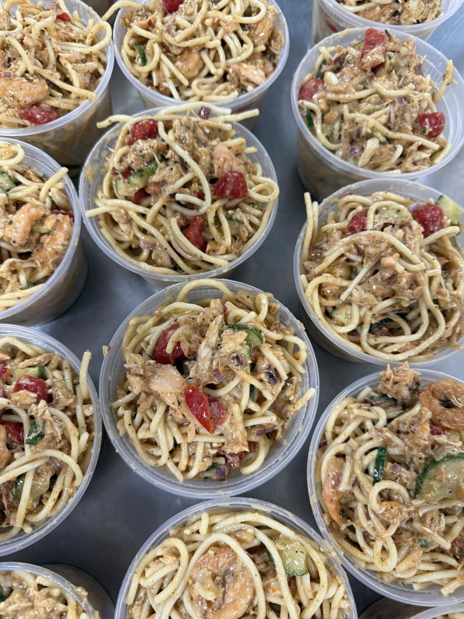Rows of cups filled with chilled seafood pasta salad, portioned for a catering order