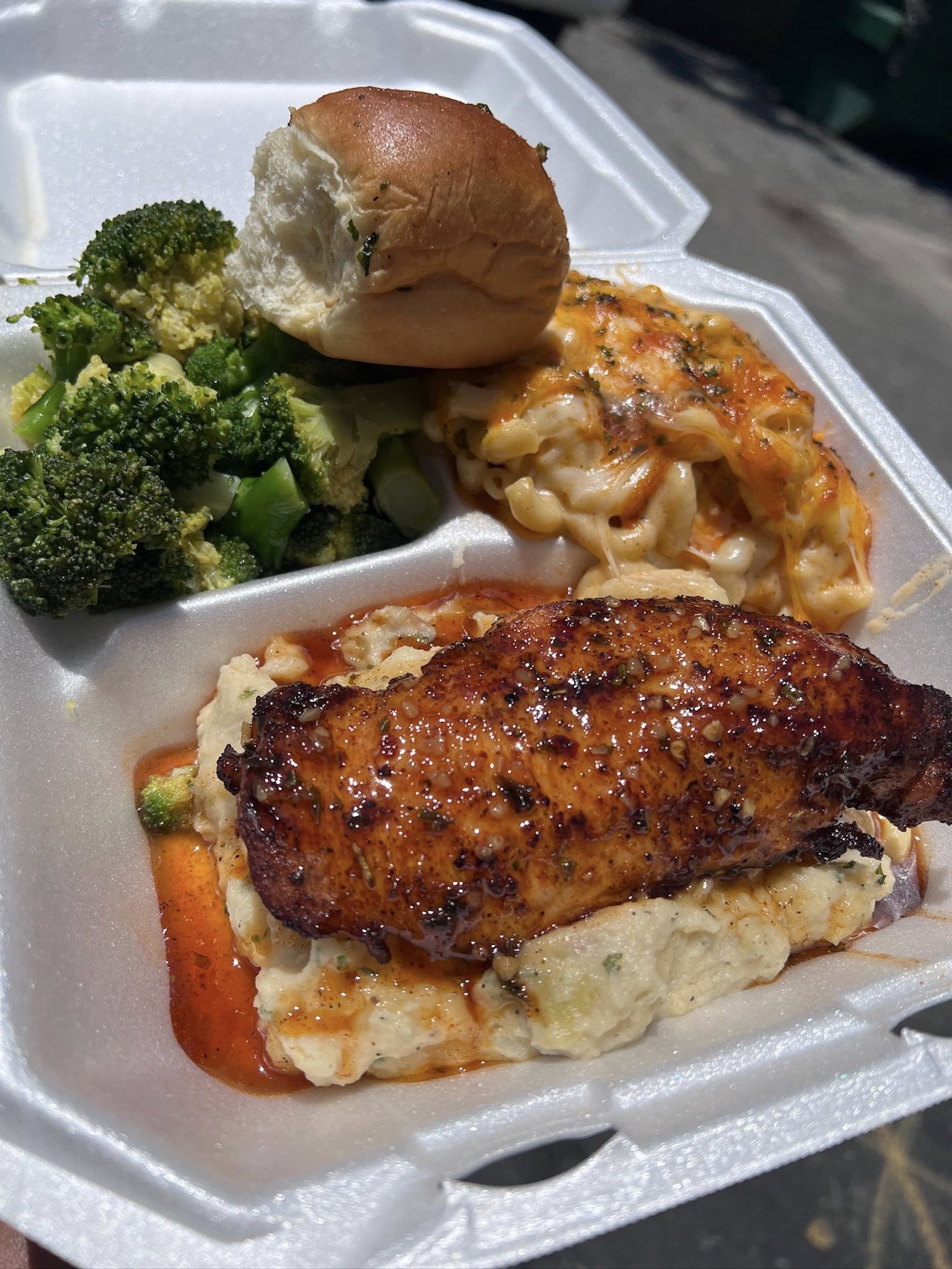 Seasoned chicken breast over garlic mashed potatoes with baked mac and cheese, steamed broccoli and a roll