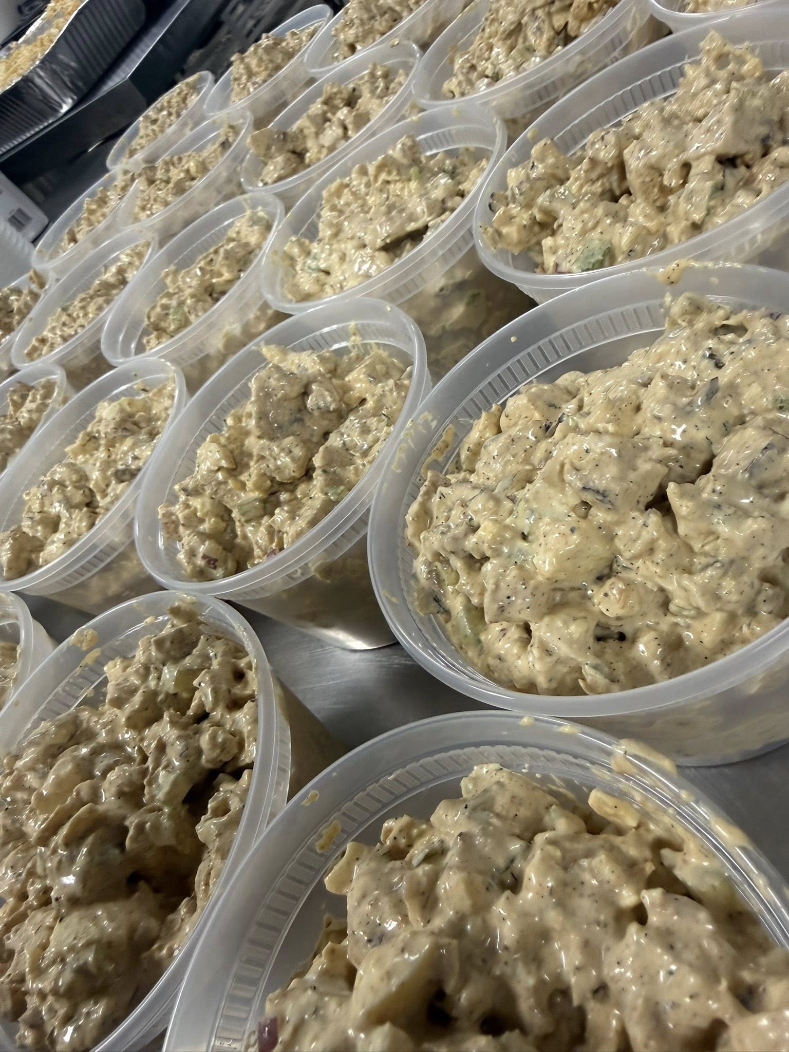 Dozens of containers of house-made chicken salad lined up on a steel prep table